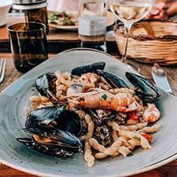Seafood pasta dish with shrimp, mussels, and squid on a blue plate.