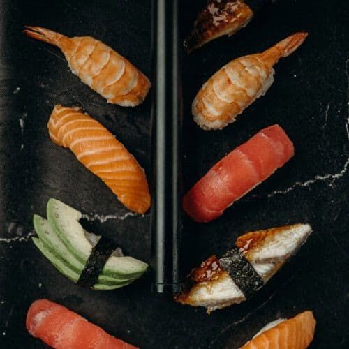 Assorted sushi rolls and sashimi on a black slate plate with chopsticks.