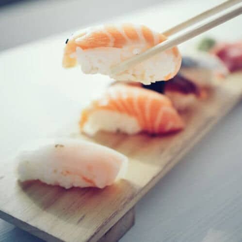 Fresh sushi pieces with salmon and white fish on a wooden serving board.