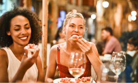 Two women enjoying pizza at a restaurant with a lively ambiance.