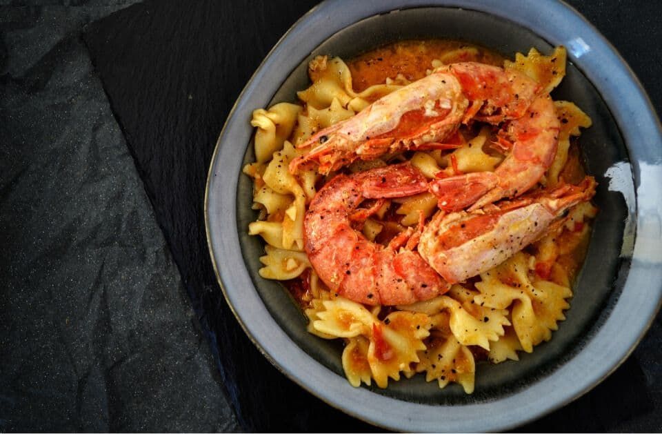 Seafood pasta with shrimp in a black bowl on a dark surface.