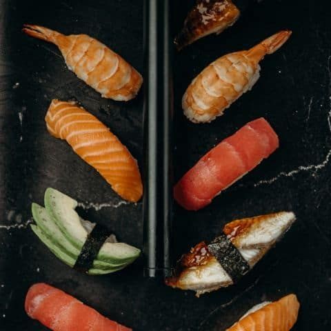 Assorted sushi pieces on a black slate serving platter with chopsticks.