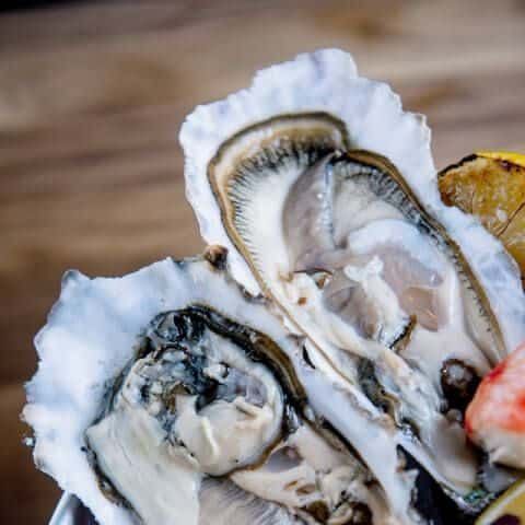 Fresh oysters on a wooden surface with lemon and garnish.