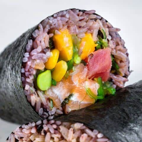 Close-up of a sushi roll with rice, vegetables, and seafood wrapped in seaweed.