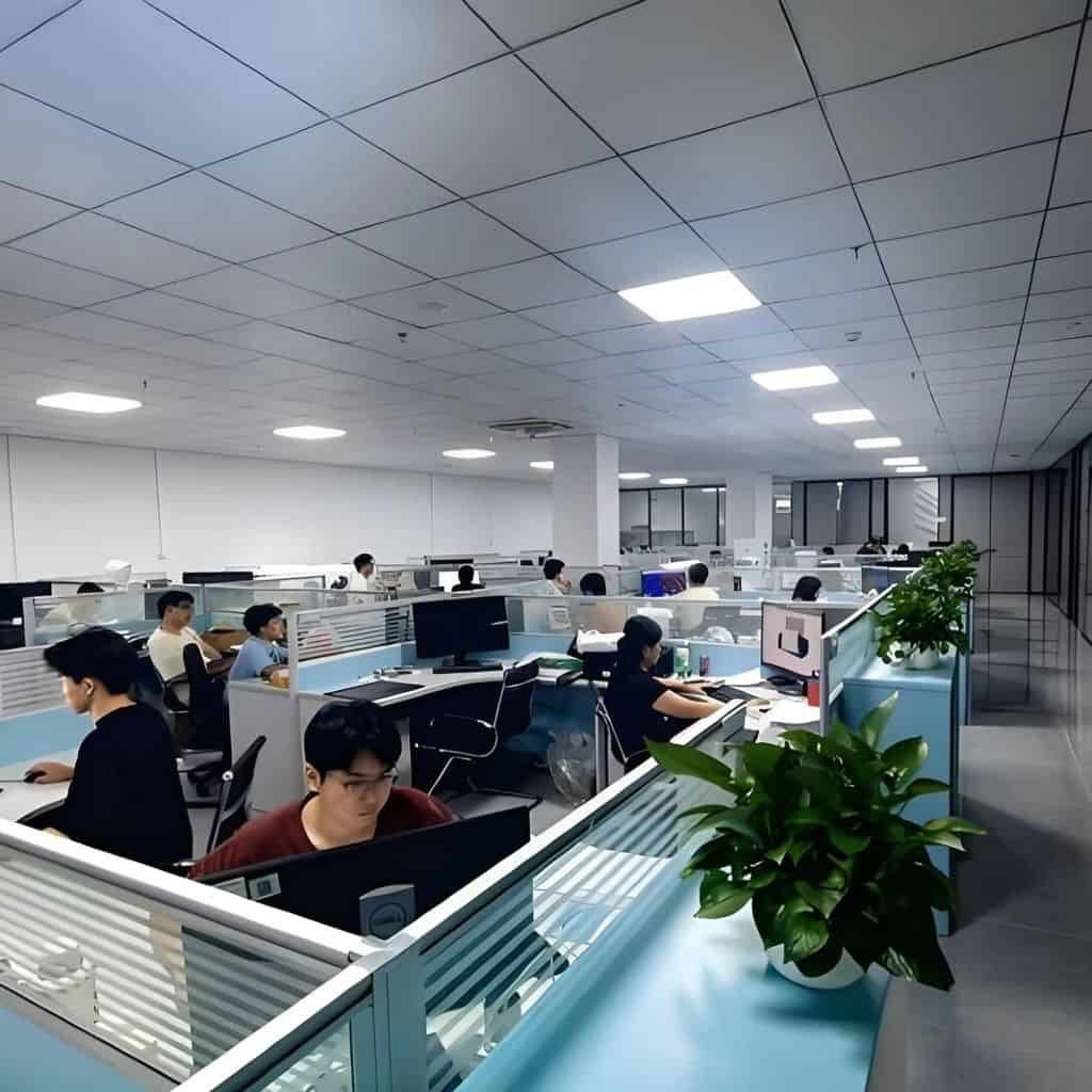 Modern office workspace with employees working at desks and plants in the foreground.