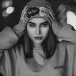 Young woman with a beanie that says 'OKAY?' in black and white photo.